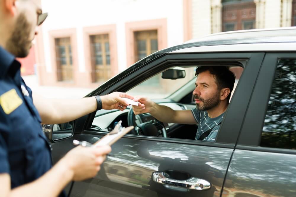 Young caucasian man giving his license and registration to a police officer to give him a parking traffic ticket